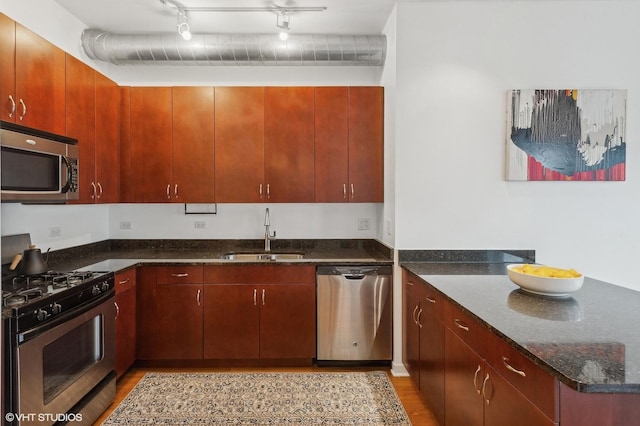 kitchen with sink, dark stone counters, track lighting, stainless steel appliances, and light hardwood / wood-style floors