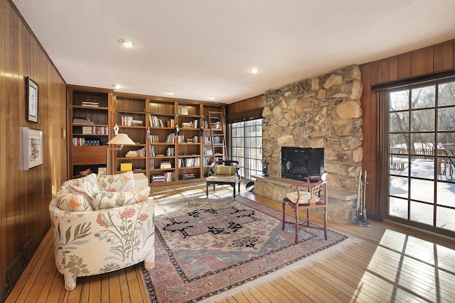 living room with a textured ceiling, a fireplace, light wood-type flooring, and wood walls