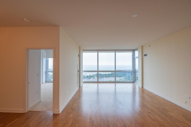 unfurnished room featuring a water view, a wall of windows, and light hardwood / wood-style flooring