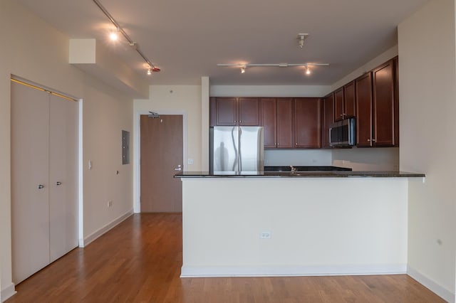 kitchen with light hardwood / wood-style floors, appliances with stainless steel finishes, dark stone counters, and kitchen peninsula