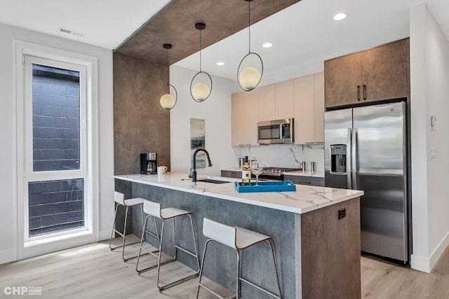 kitchen with light stone counters, decorative light fixtures, light hardwood / wood-style flooring, kitchen peninsula, and stainless steel appliances