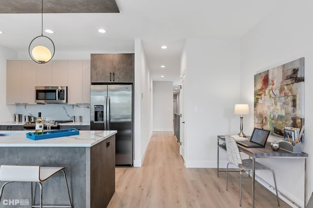 kitchen featuring appliances with stainless steel finishes, tasteful backsplash, hanging light fixtures, light stone countertops, and light wood-type flooring