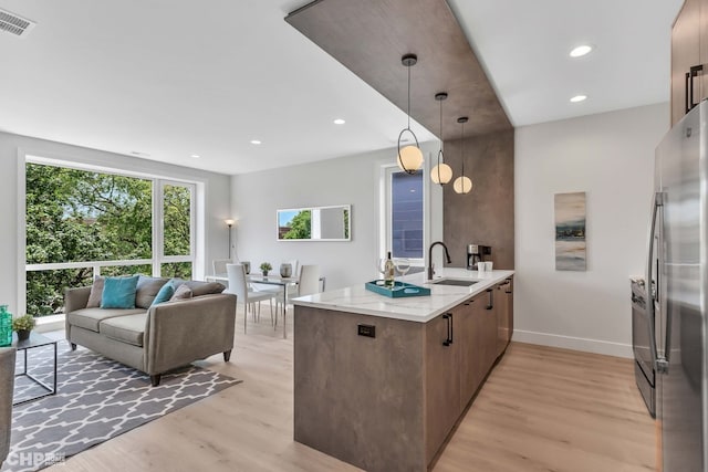 kitchen featuring sink, decorative light fixtures, light hardwood / wood-style flooring, stainless steel fridge, and kitchen peninsula