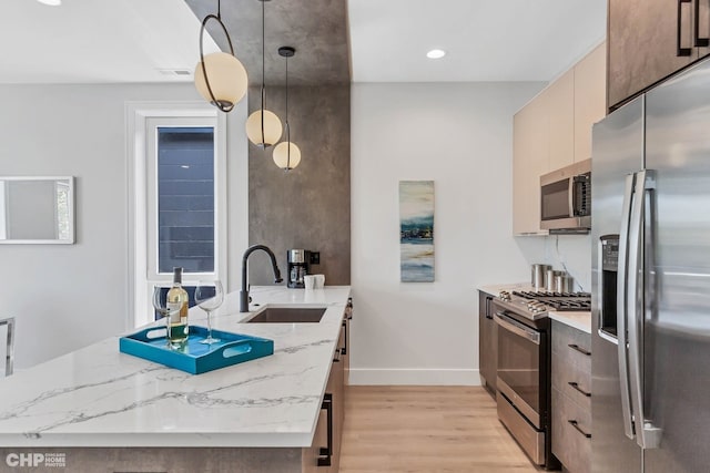 kitchen with appliances with stainless steel finishes, pendant lighting, sink, light stone counters, and light hardwood / wood-style flooring