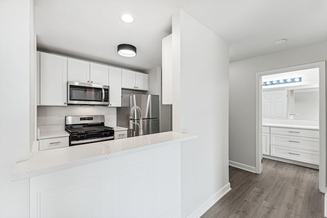 kitchen featuring light stone countertops, appliances with stainless steel finishes, wood-type flooring, and white cabinets