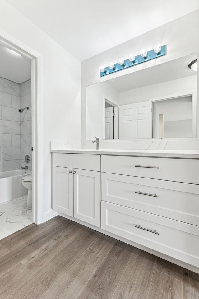 full bathroom with tiled shower / bath, vanity, toilet, and hardwood / wood-style floors