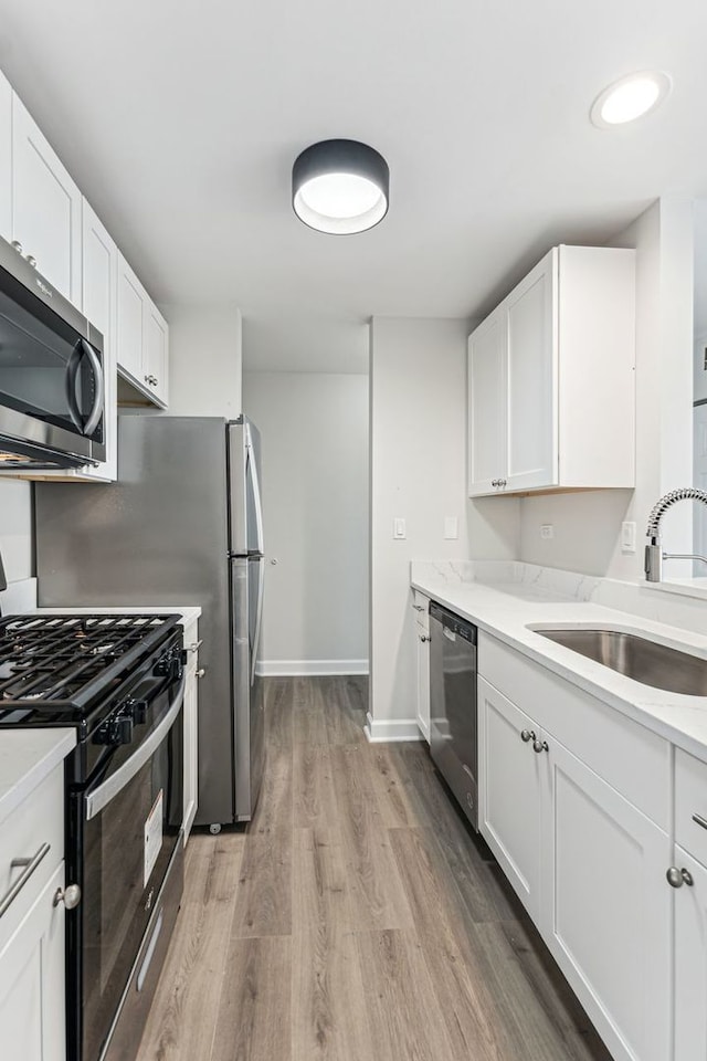 kitchen featuring white cabinetry, sink, stainless steel appliances, light stone countertops, and light hardwood / wood-style flooring