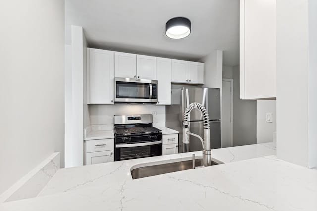 kitchen featuring white cabinetry, appliances with stainless steel finishes, light stone countertops, and sink