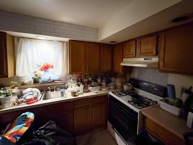 kitchen with tasteful backsplash, white gas range, sink, and tile patterned flooring