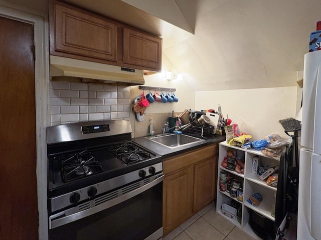 kitchen with lofted ceiling, sink, stainless steel gas range oven, light tile patterned floors, and decorative backsplash