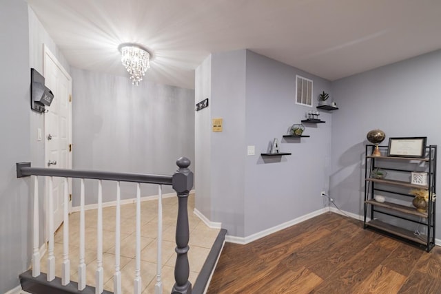 stairs with an inviting chandelier, baseboards, visible vents, and wood finished floors