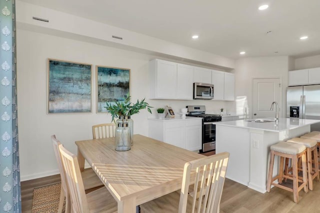 kitchen featuring sink, appliances with stainless steel finishes, white cabinetry, light hardwood / wood-style floors, and an island with sink