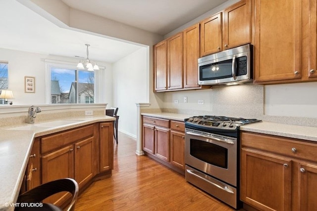 kitchen featuring sink, pendant lighting, stainless steel appliances, light hardwood / wood-style floors, and backsplash