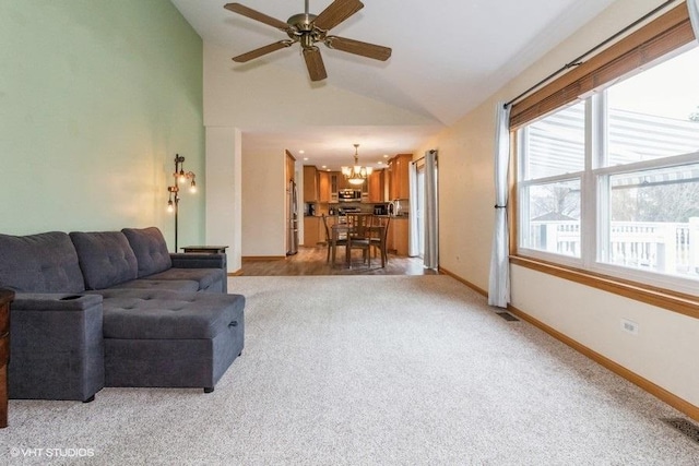 carpeted living room with ceiling fan with notable chandelier and high vaulted ceiling