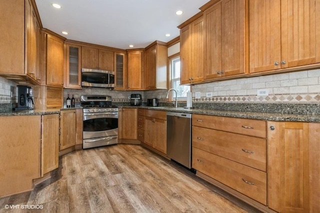 kitchen featuring backsplash, appliances with stainless steel finishes, light wood-type flooring, and dark stone countertops