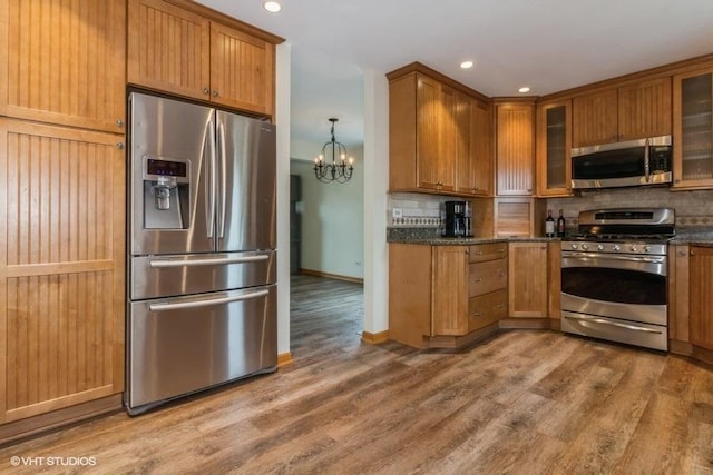 kitchen featuring appliances with stainless steel finishes, hardwood / wood-style floors, tasteful backsplash, a notable chandelier, and dark stone counters