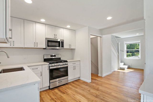 kitchen with sink, white cabinets, light hardwood / wood-style floors, stainless steel appliances, and light stone countertops