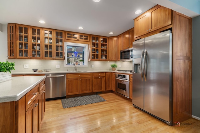 kitchen with sink, decorative backsplash, light wood-type flooring, and appliances with stainless steel finishes