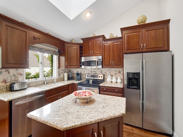 kitchen featuring sink, a kitchen island, stainless steel appliances, vaulted ceiling with skylight, and backsplash