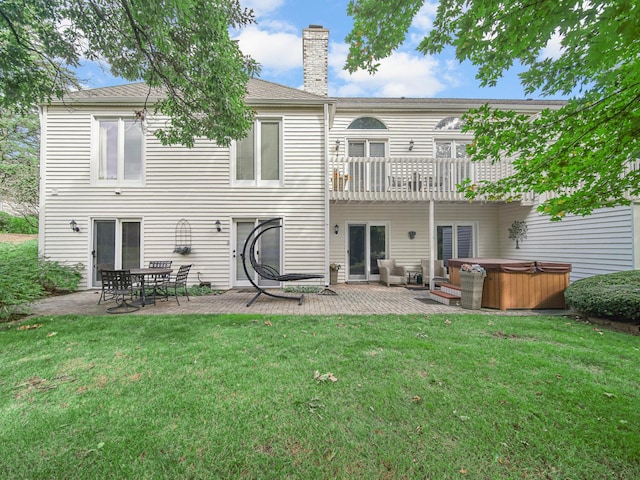 rear view of house featuring a balcony, a hot tub, a patio, and a lawn