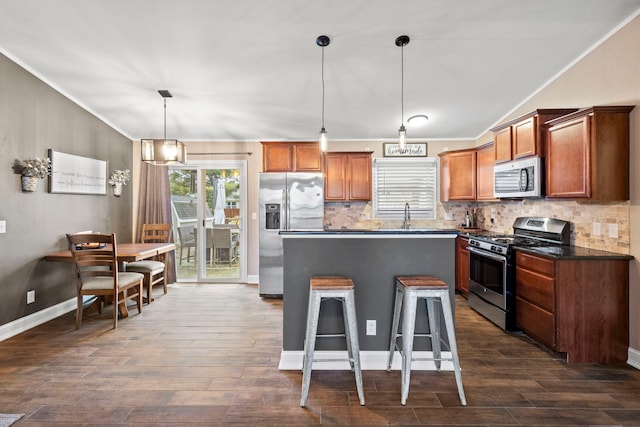 kitchen featuring appliances with stainless steel finishes, a kitchen breakfast bar, hanging light fixtures, ornamental molding, and dark wood-type flooring