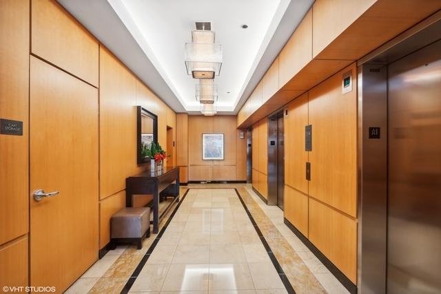 hallway with a tray ceiling, elevator, and light tile patterned flooring