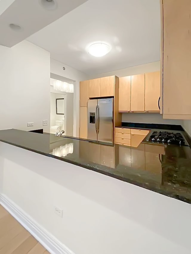 kitchen with kitchen peninsula, stainless steel fridge, light brown cabinetry, and black gas cooktop