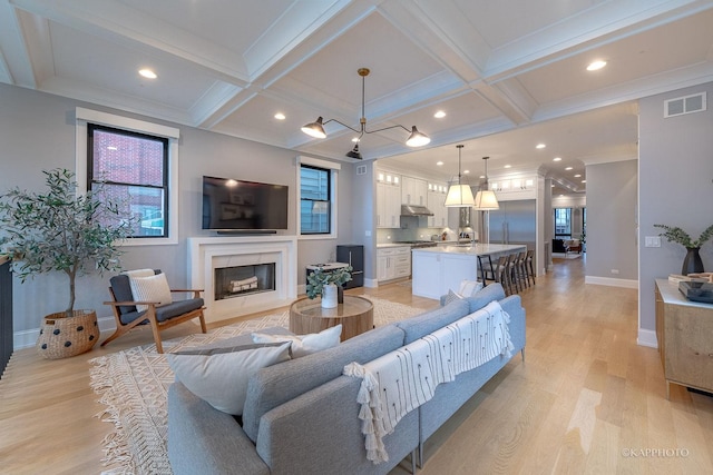 living room with coffered ceiling, light hardwood / wood-style flooring, ornamental molding, a high end fireplace, and beam ceiling