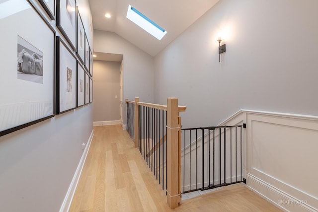 hallway with lofted ceiling with skylight and light hardwood / wood-style floors