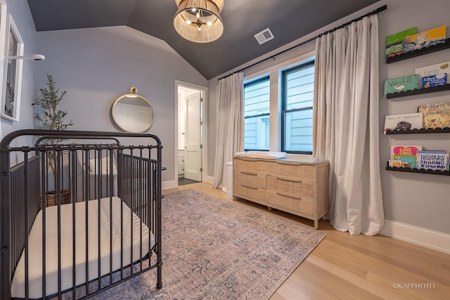 bedroom with lofted ceiling, a nursery area, and light wood-type flooring