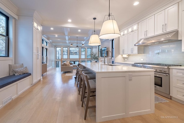 kitchen featuring pendant lighting, a breakfast bar area, white cabinets, high end range, and a kitchen island with sink