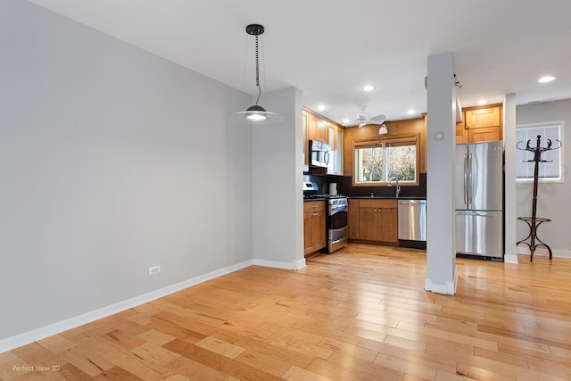 kitchen featuring stainless steel appliances, sink, light wood-type flooring, and decorative light fixtures