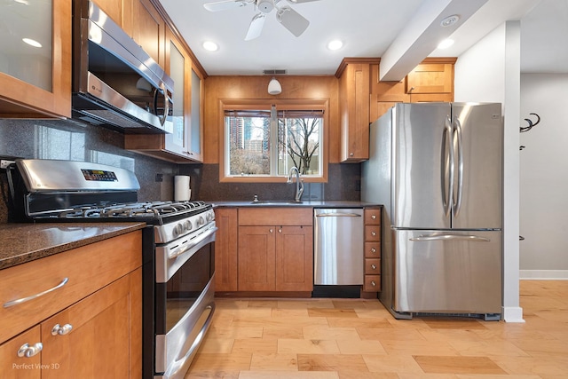 kitchen featuring sink, dark stone counters, ceiling fan, stainless steel appliances, and decorative backsplash