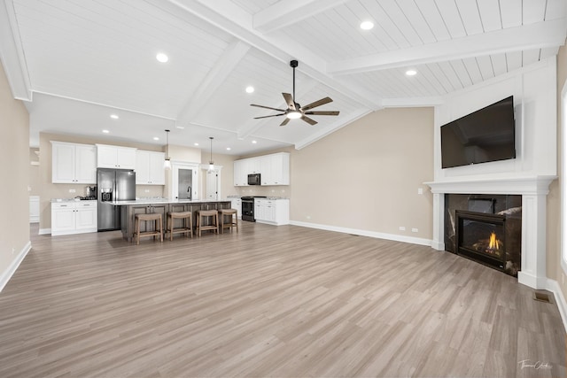 unfurnished living room with lofted ceiling with beams, a large fireplace, sink, and light hardwood / wood-style flooring