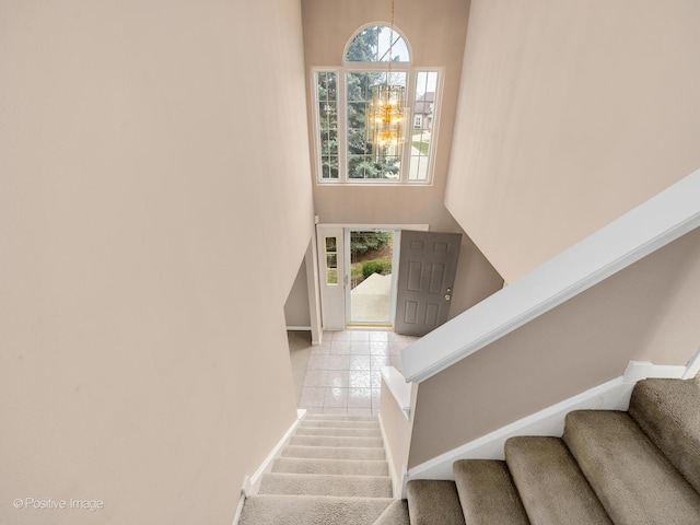 stairway with tile patterned floors, a chandelier, and a high ceiling