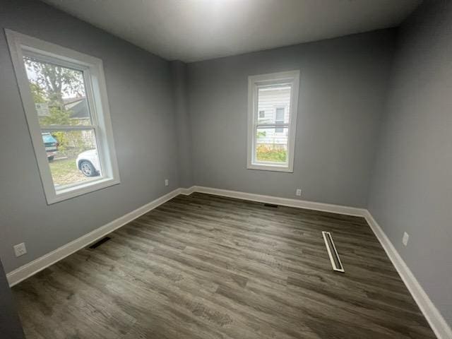 empty room with a wealth of natural light and dark hardwood / wood-style floors