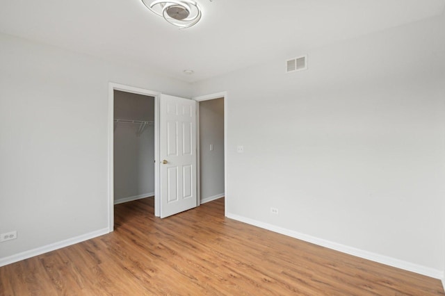 unfurnished bedroom with a spacious closet, a closet, and light wood-type flooring