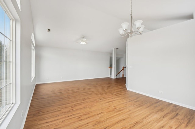 empty room featuring lofted ceiling, ceiling fan with notable chandelier, and light wood-type flooring