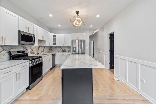 kitchen featuring white cabinetry, a center island, appliances with stainless steel finishes, pendant lighting, and light stone countertops