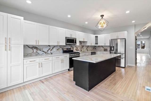 kitchen with pendant lighting, white cabinetry, stainless steel appliances, a center island, and light stone counters