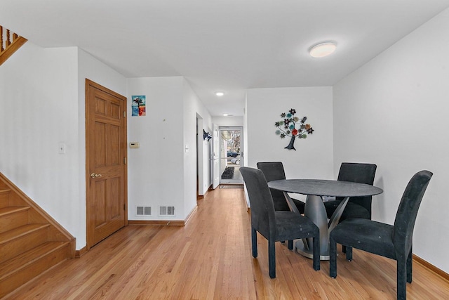 dining area featuring light wood-style flooring, stairs, baseboards, and visible vents