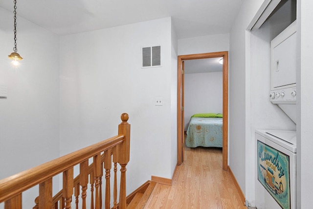 hallway with light wood finished floors, stacked washer / drying machine, visible vents, an upstairs landing, and baseboards