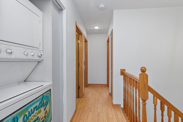 hallway featuring stacked washer and dryer, an upstairs landing, baseboards, light wood-type flooring, and attic access