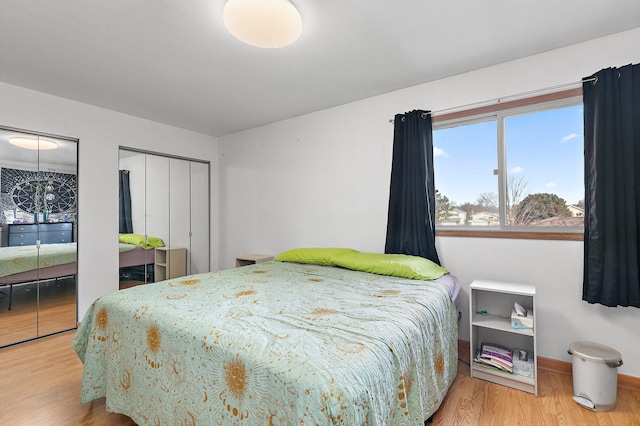 bedroom featuring wood finished floors, two closets, and baseboards