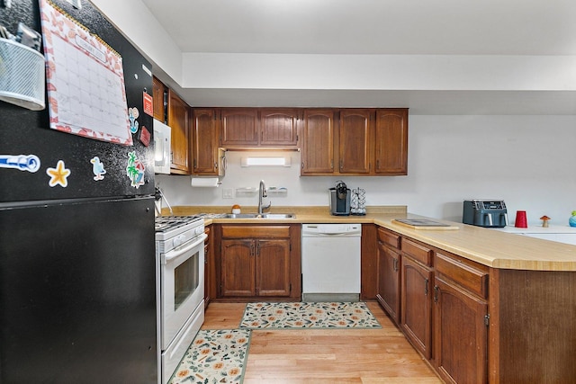 kitchen featuring light countertops, a sink, light wood-type flooring, white appliances, and a peninsula