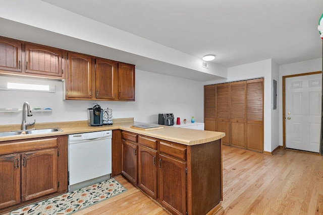 kitchen with white dishwasher, a peninsula, a sink, light countertops, and light wood finished floors