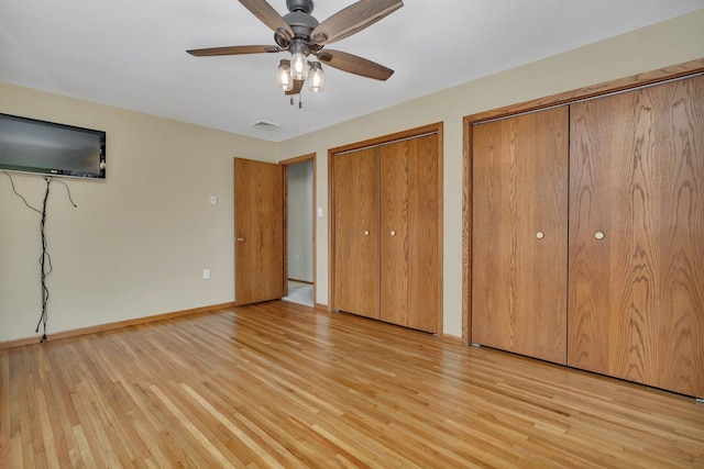 unfurnished bedroom featuring ceiling fan, multiple closets, and light wood-type flooring