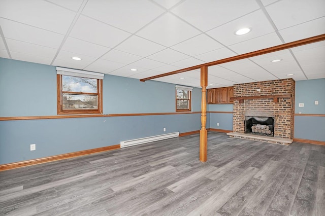 unfurnished living room featuring a drop ceiling, a brick fireplace, a baseboard radiator, and light hardwood / wood-style floors