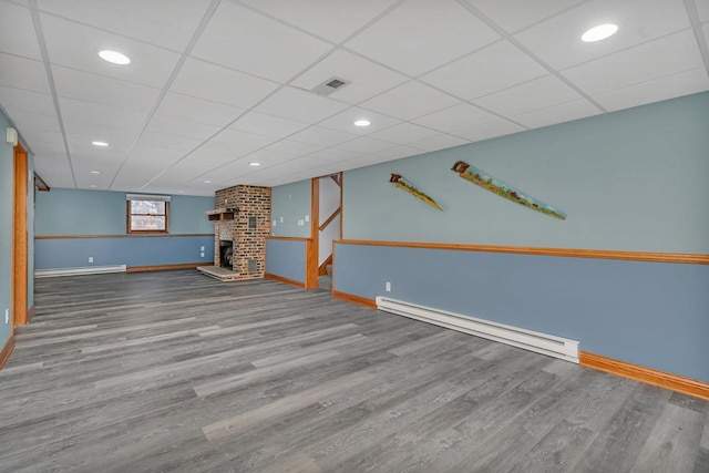 basement featuring hardwood / wood-style flooring, a baseboard radiator, a fireplace, and a drop ceiling