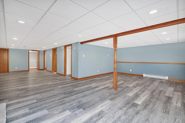 basement featuring a drop ceiling, wood-type flooring, and baseboard heating